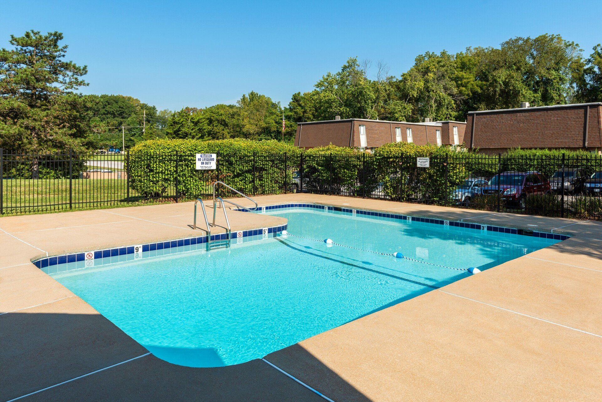 Outdoor swimming pool with blue water, tan deck, and trees in the background