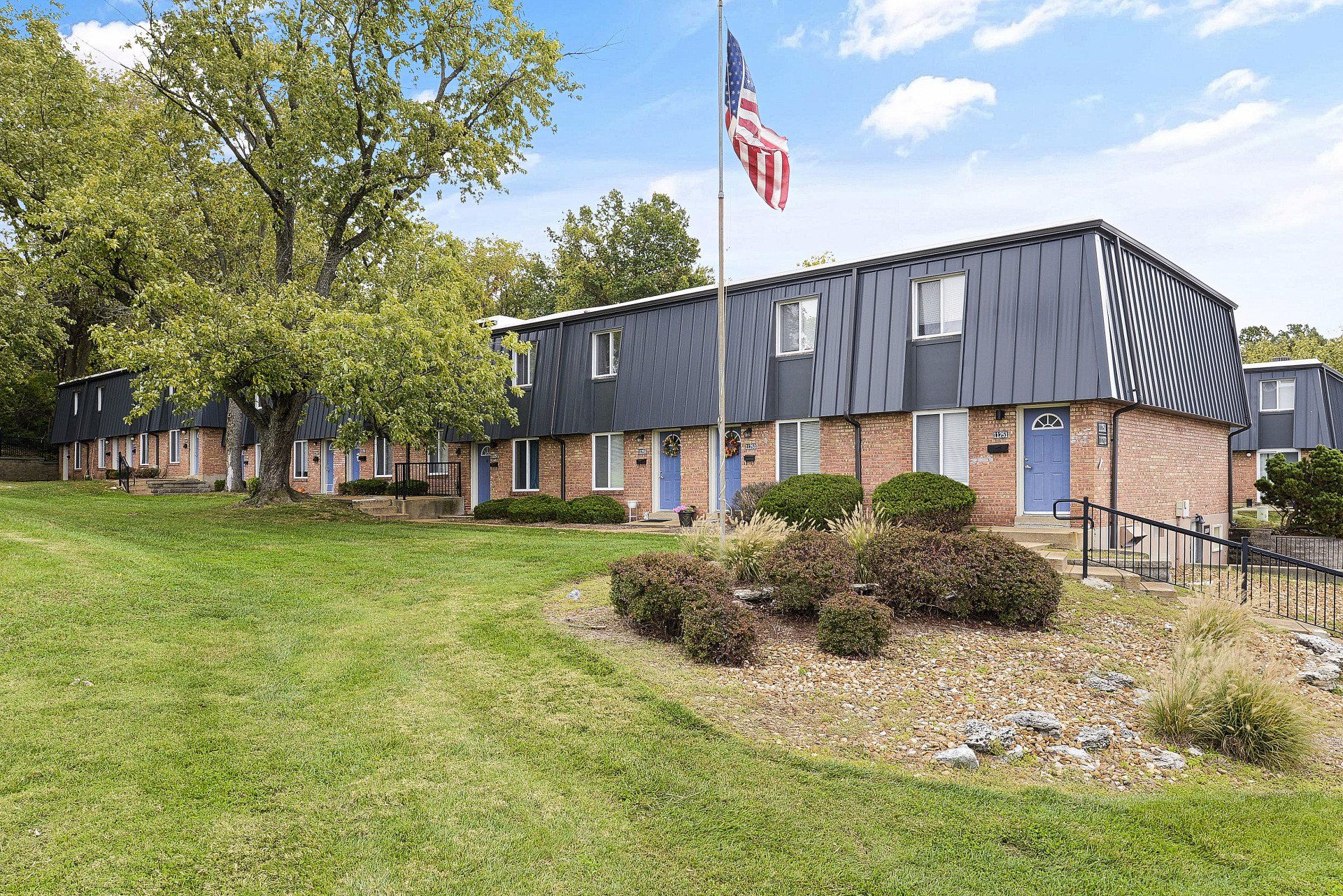 Apartment building with dark siding, American flag, and landscaped lawn on a sunny day