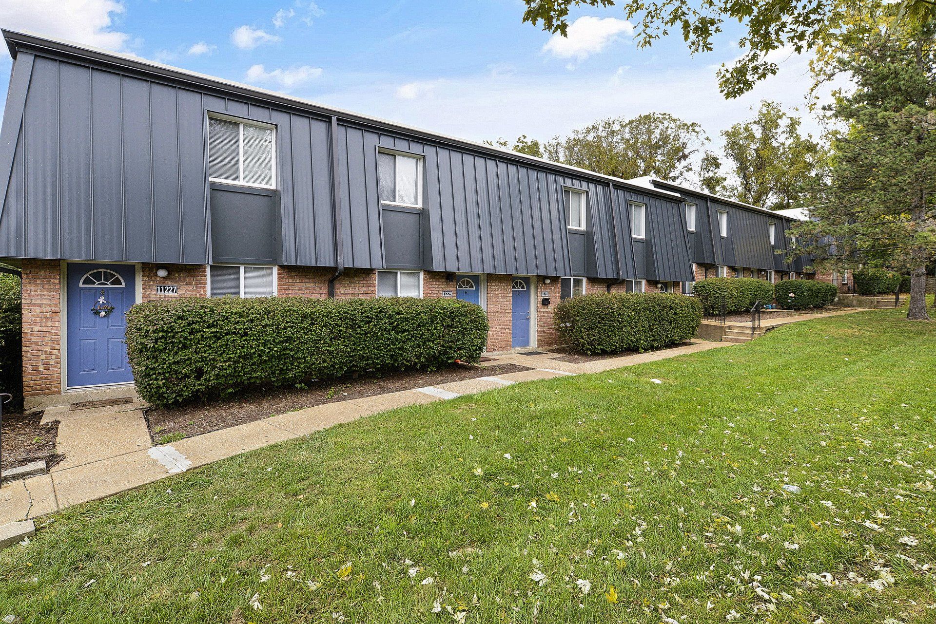 Row of brick townhouses with dark siding, blue doors, and a grassy front lawn under a cloudy sky