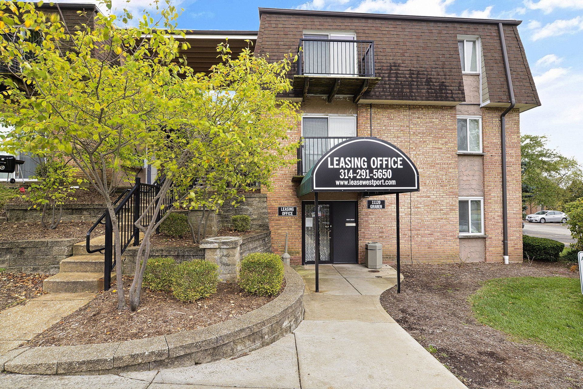 Brick office building with a black awning and a front walkway, surrounded by trees and landscaping