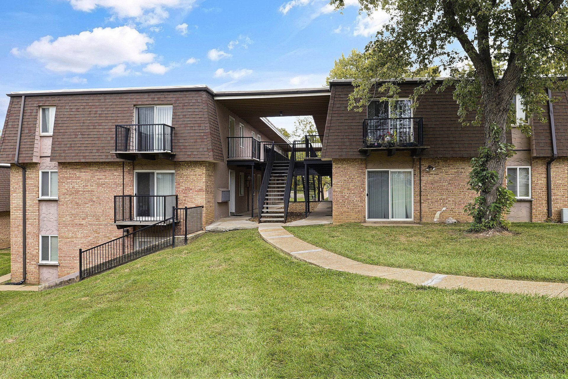 Brick apartment building with balconies and a grassy courtyard under a partly cloudy sky
