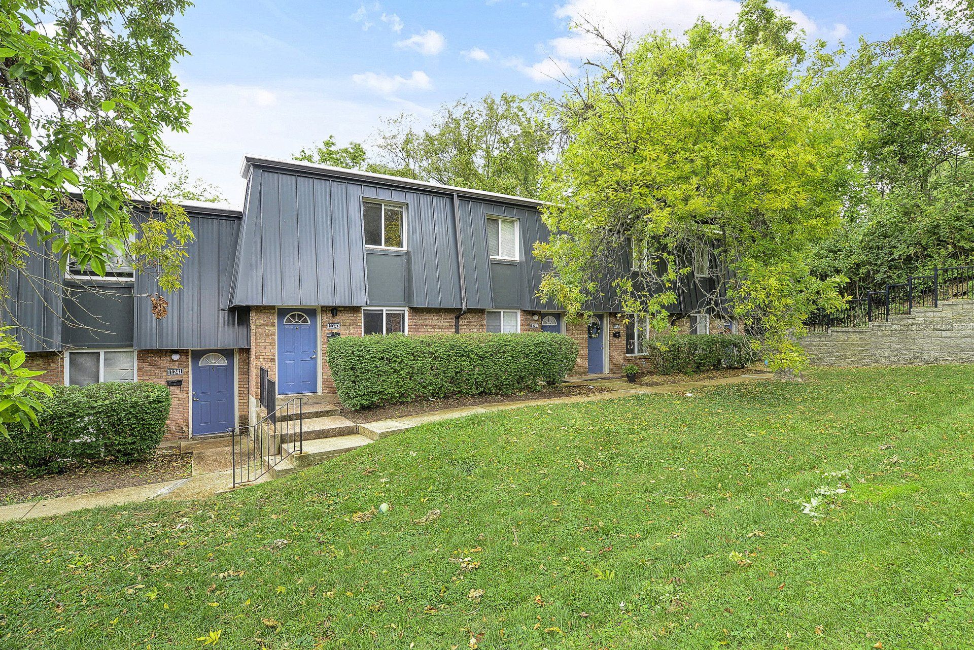 Apartment building with blue door beside a grassy lawn and trees