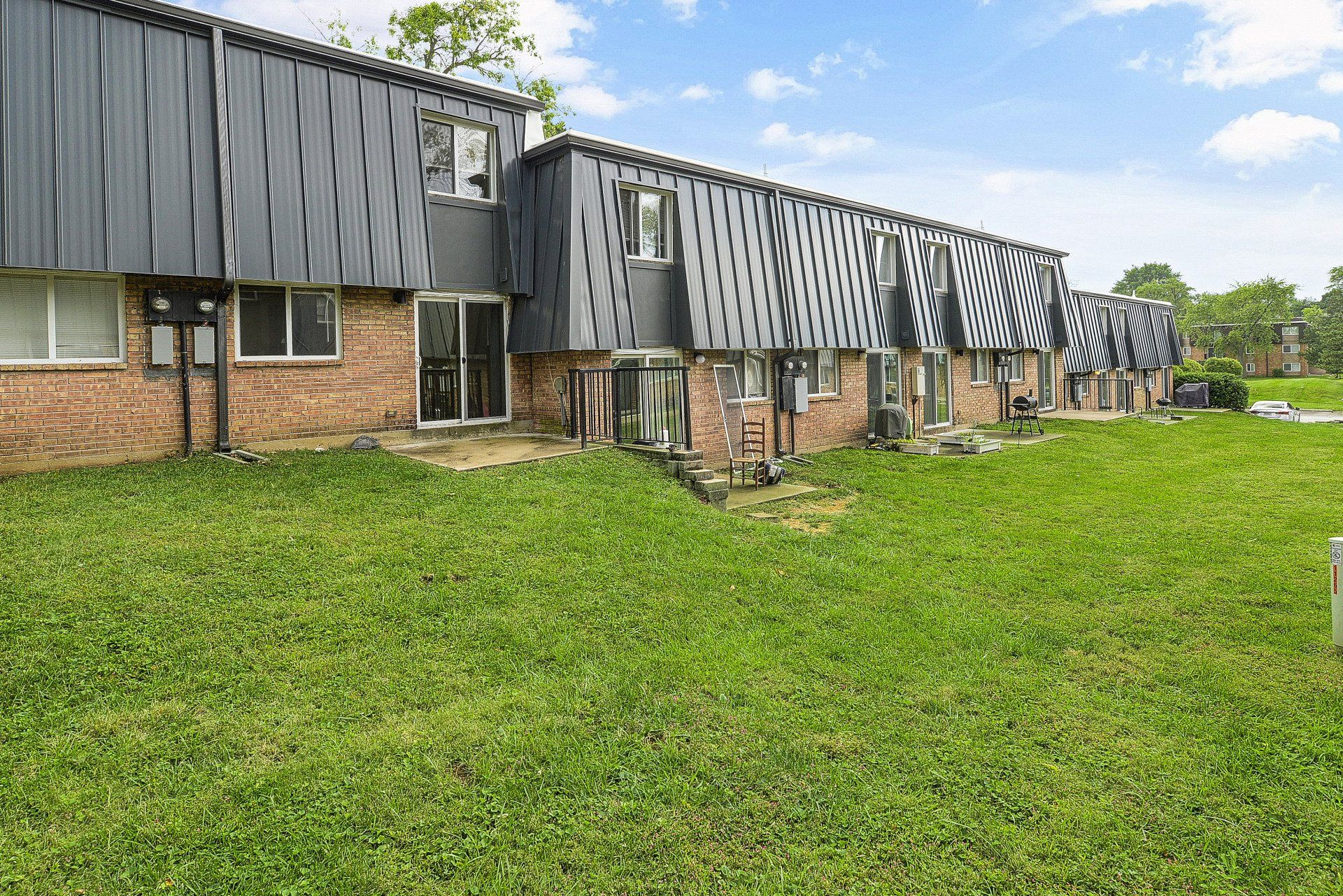 Row of dark-sided apartment buildings beside a large green lawn under a partly cloudy sky
