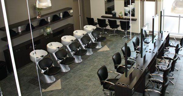 Modern hair salon with black styling chairs, mirrored stations, and shampoo basins.