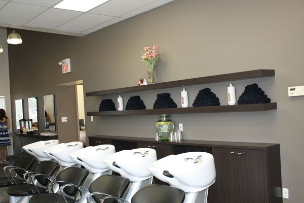 Salon interior with shampoo sinks, styling chairs, black shelves, and a cabinet along the wall