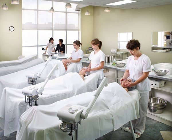 People receiving facials in a bright spa treatment room with white recliners and attendants nearby