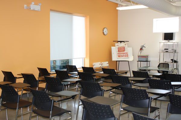 Empty classroom with rows of black chairs, orange walls, and a whiteboard at the front.