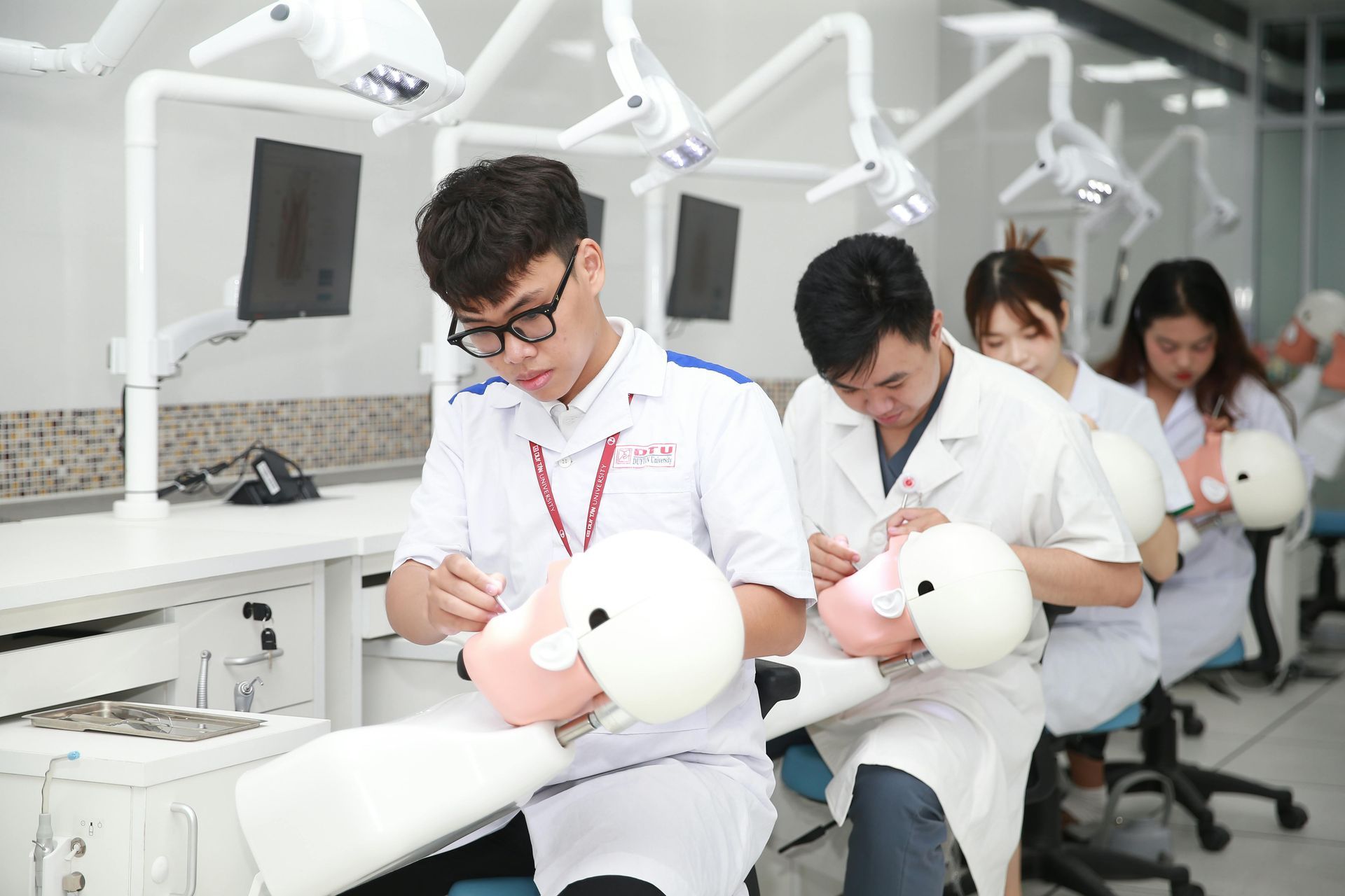 Students assembling robots in a bright engineering lab, seated at workstations with tools and monitors.