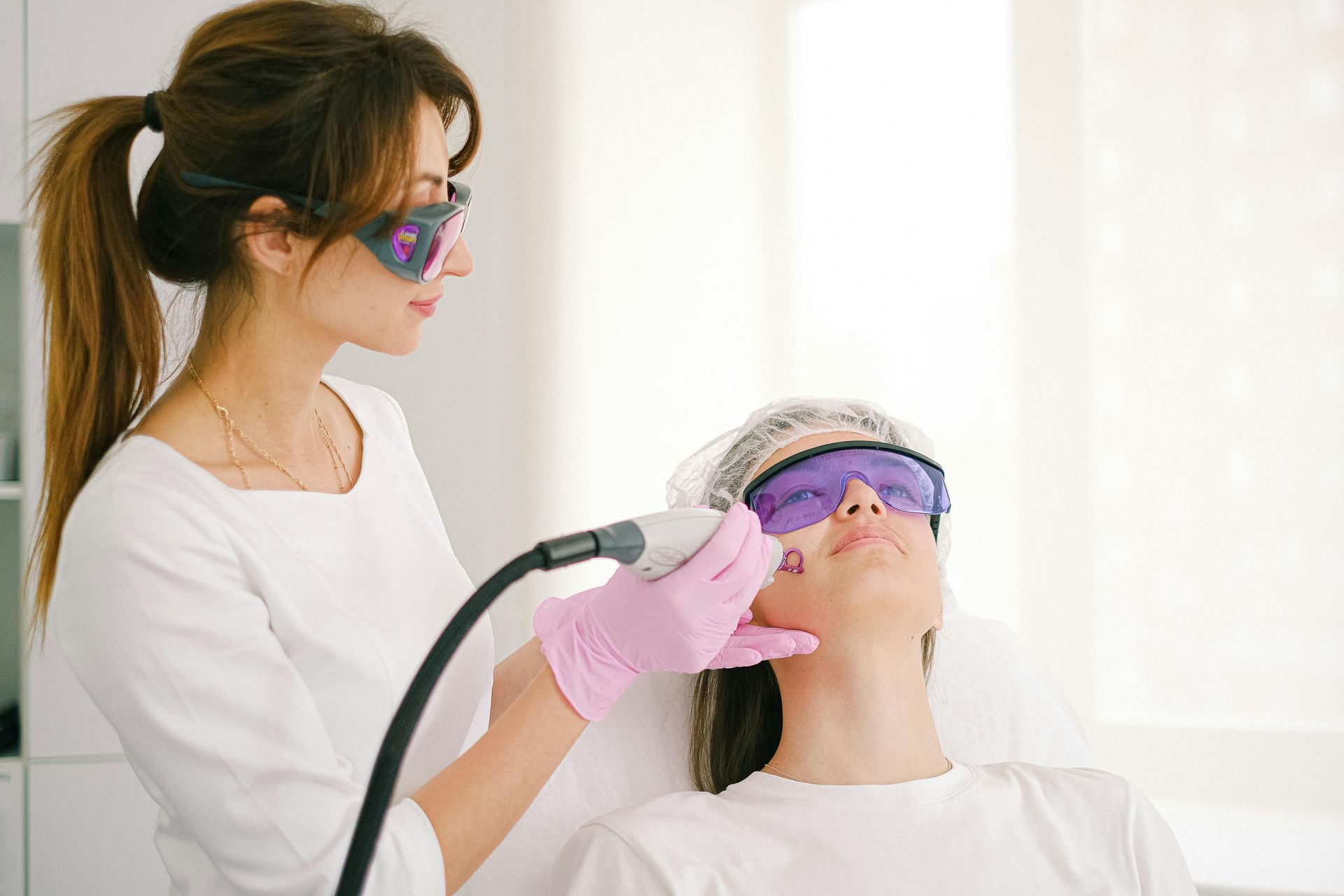 Aesthetic treatment with a clinician using a handheld device on a reclining client wearing protective goggles.