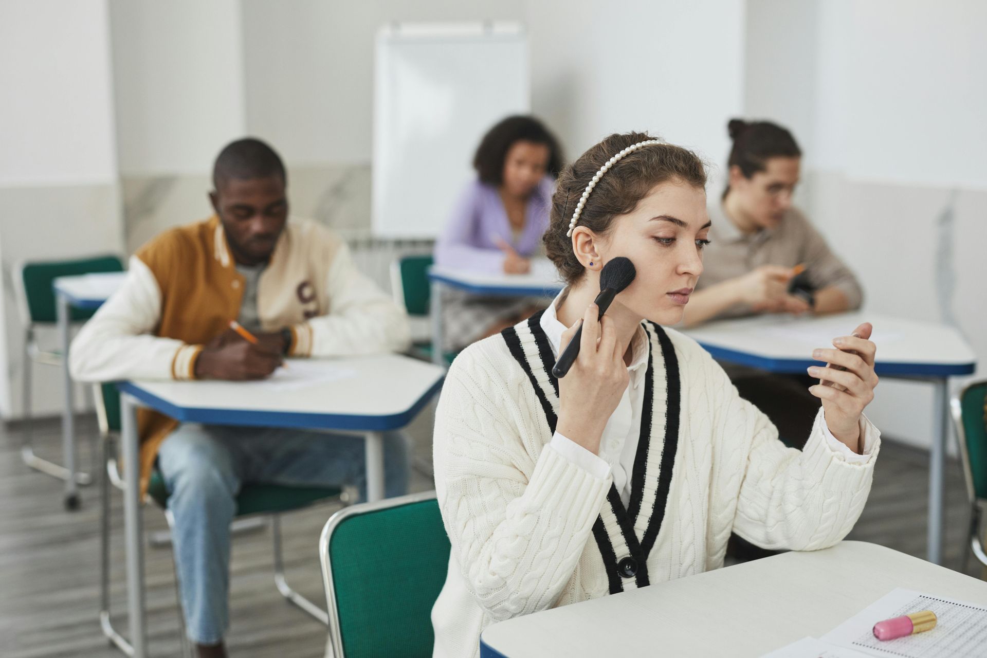 Student applying makeup in a classroom while others work at desks in the background
