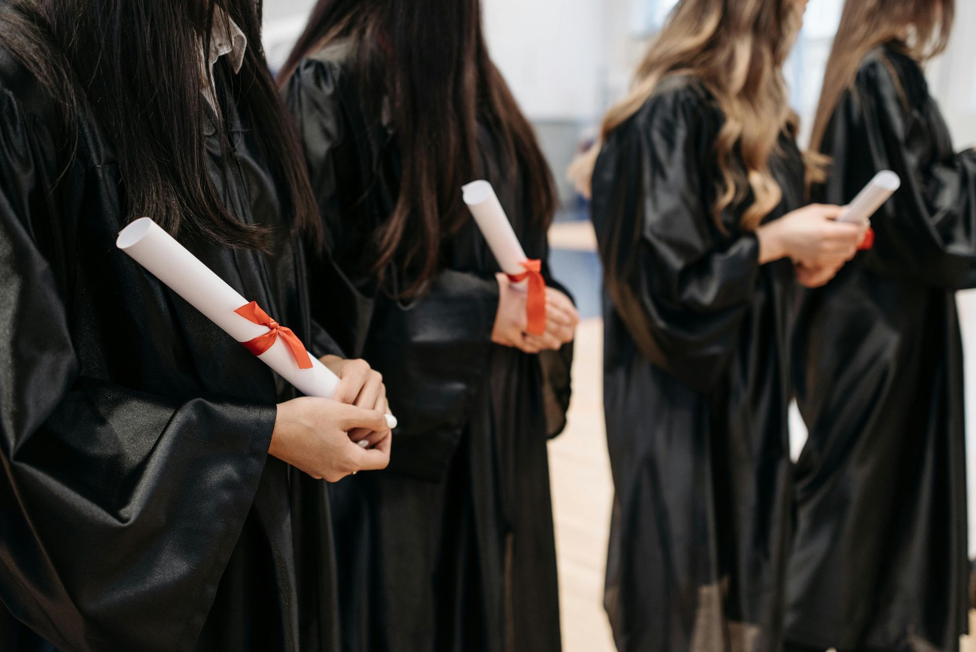 Graduates in black gowns holding rolled diplomas with red ribbons at a ceremony