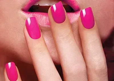Close-up of pink manicured nails held near glossy pink lips.