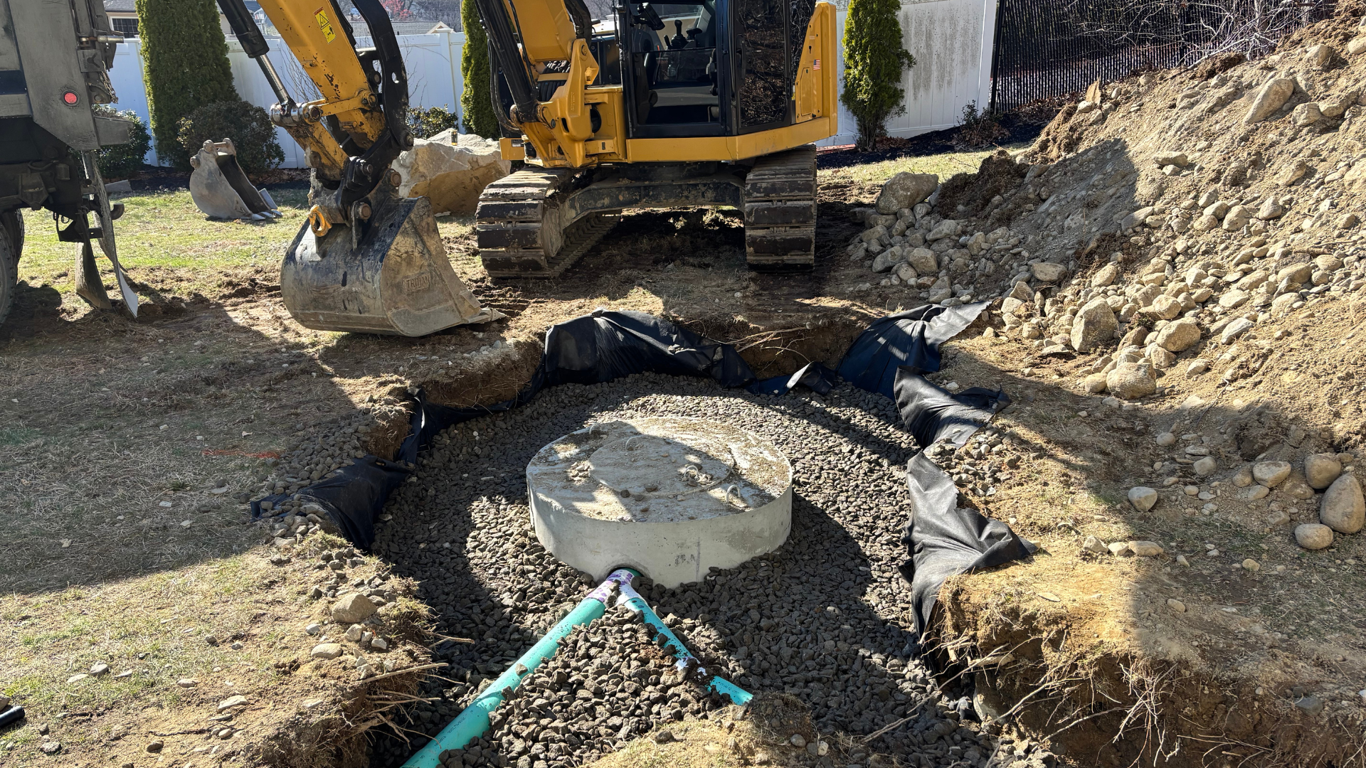 A trench in a yard with a green pipe, gravel, and black fabric for drainage.