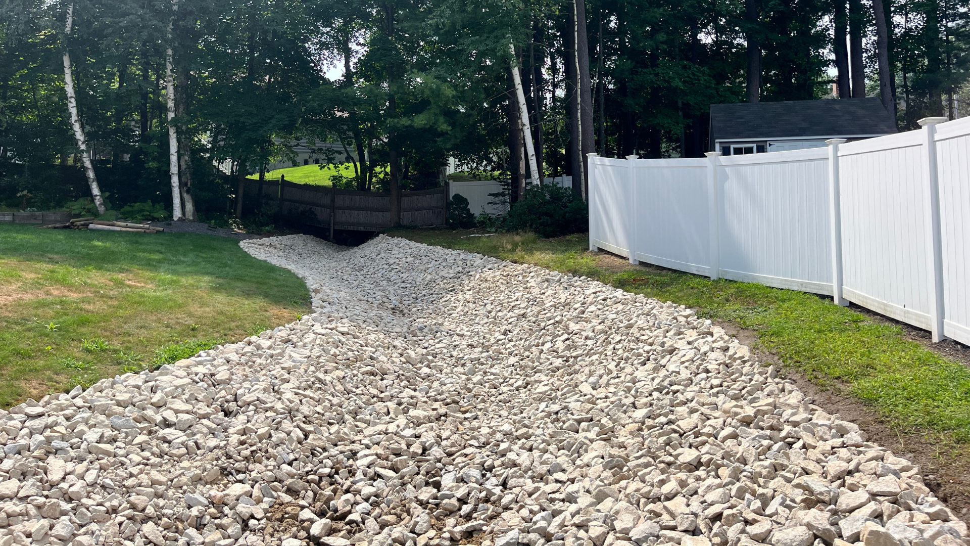 A trench in a yard with a green pipe, gravel, and black fabric for drainage.