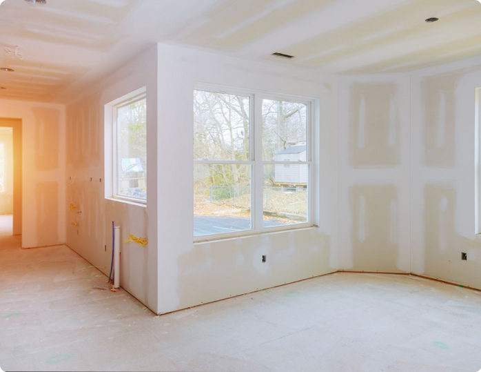 An empty room with drywall and windows in a house under construction.