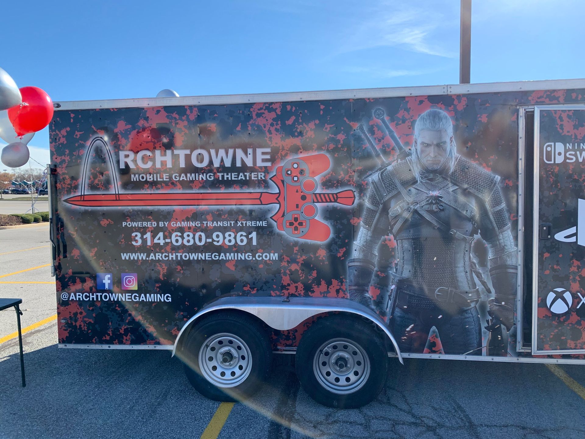 Black trailer wrap advertising ArchTowne with phone number, red balloons, and a soldier graphic at an outdoor event