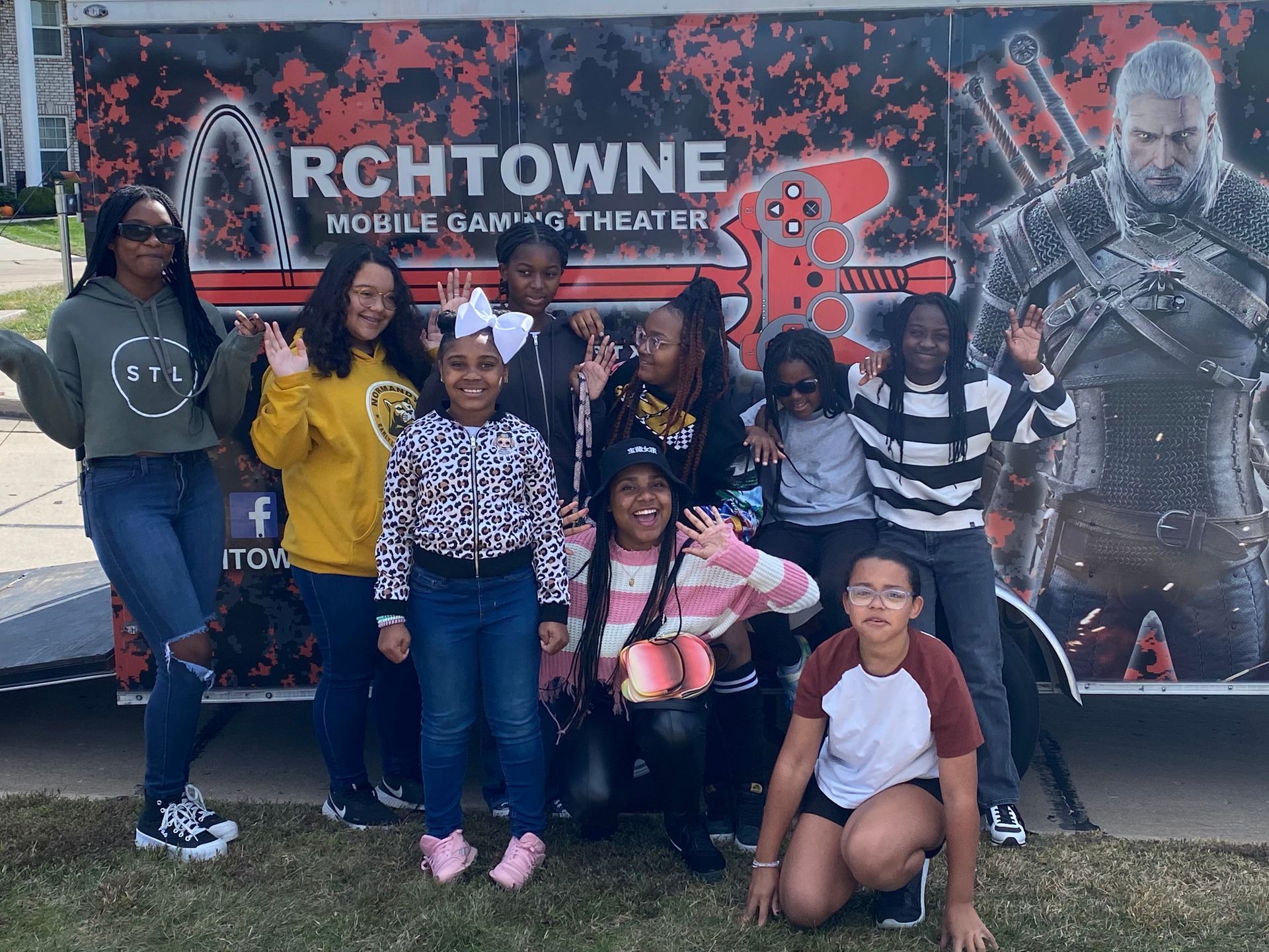 Group posing in front of an Arch Towne movie theater banner with superhero artwork.