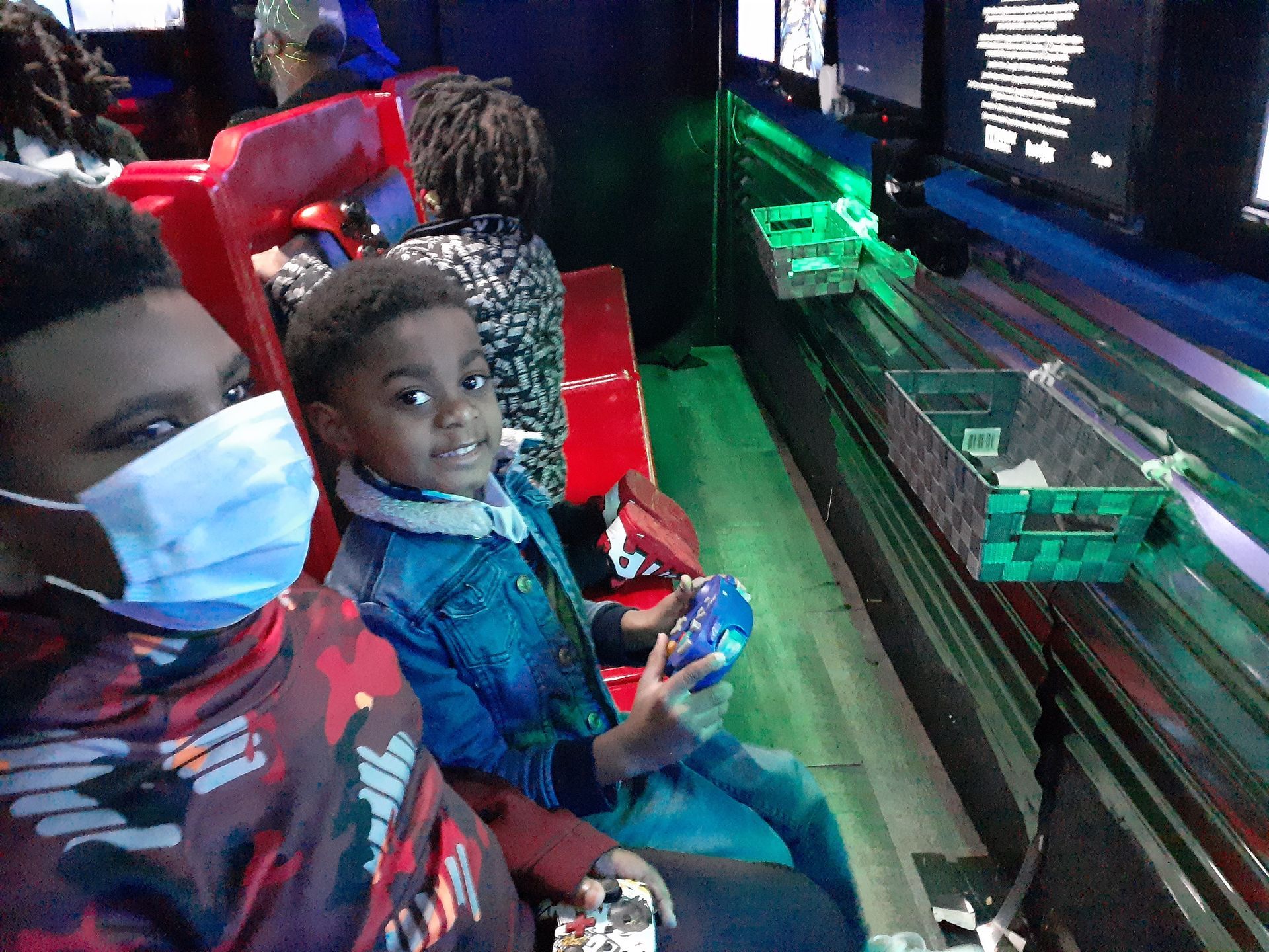 Children seated in red arcade chairs, looking at a lit screen in a dark gaming area
