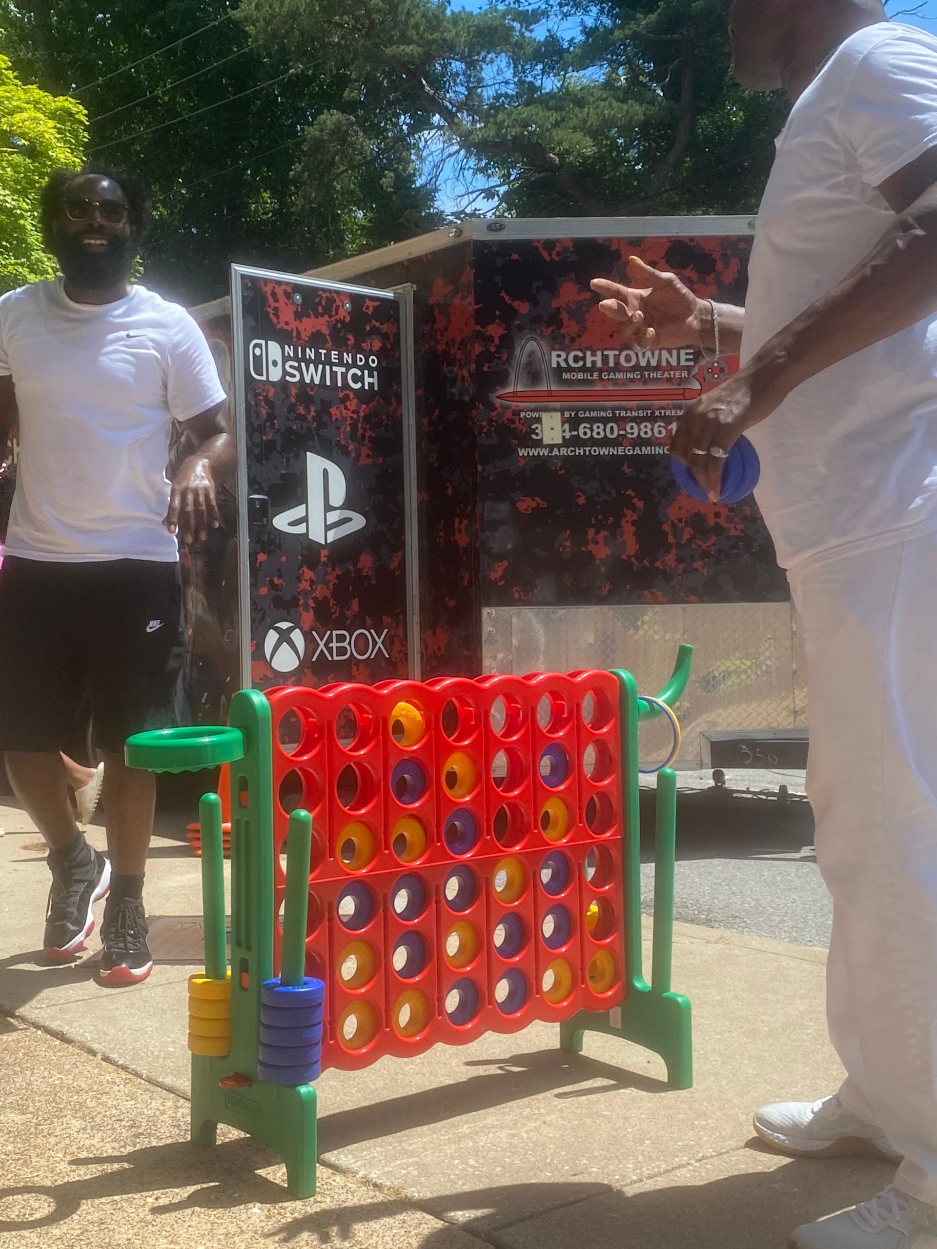 Large Connect Four game outdoors with two people standing beside it and a PlayStation-branded backdrop