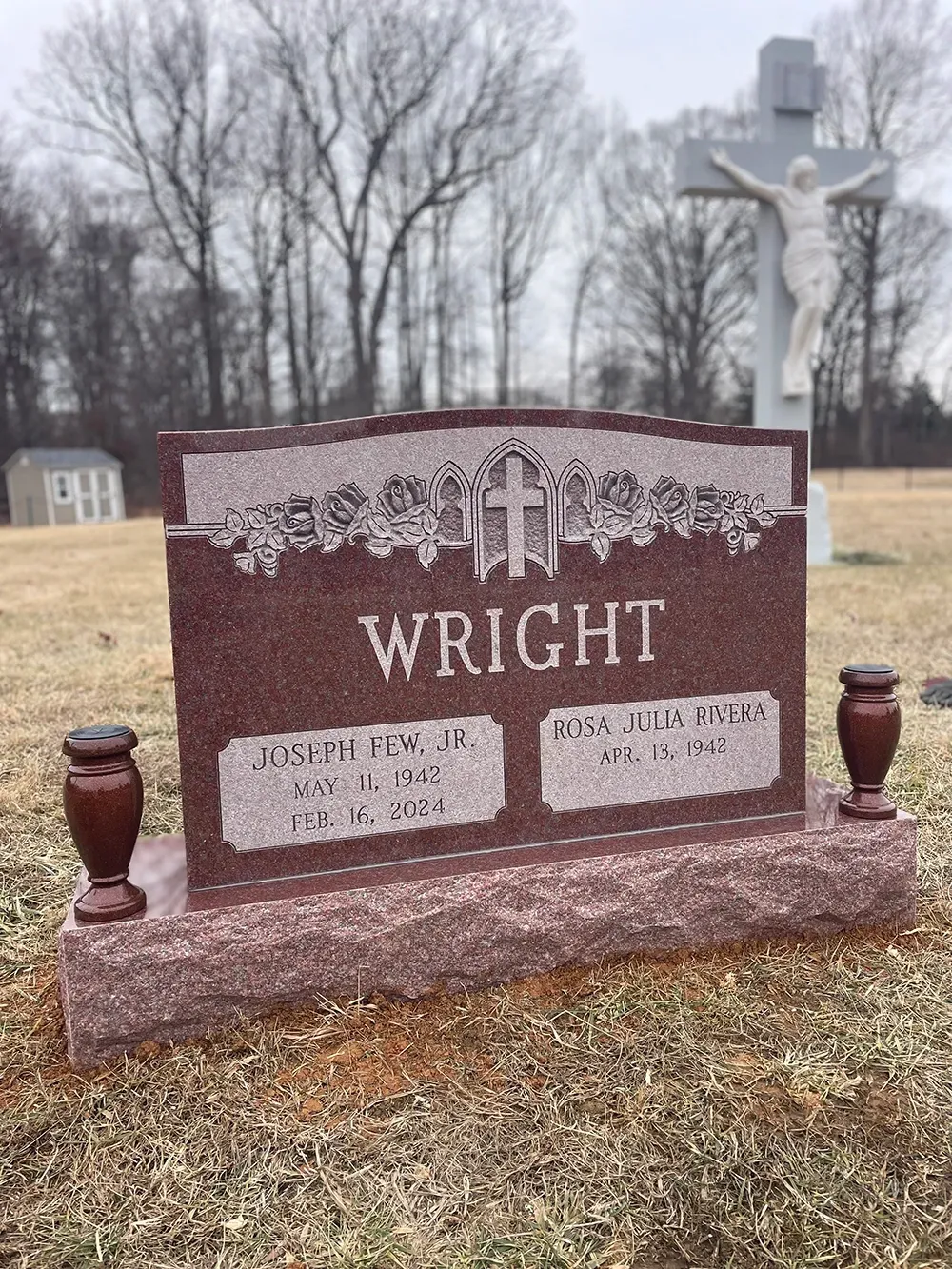 A red granite upright cemetery monument for the Wright family, featuring a central cross, with a large crucifix behind.