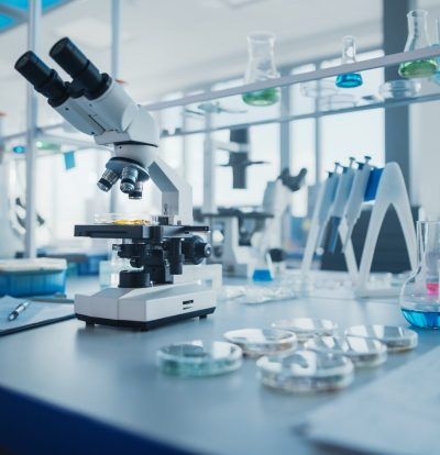 Microscope on lab bench with petri dishes and scientific equipment in a bright lab setting.