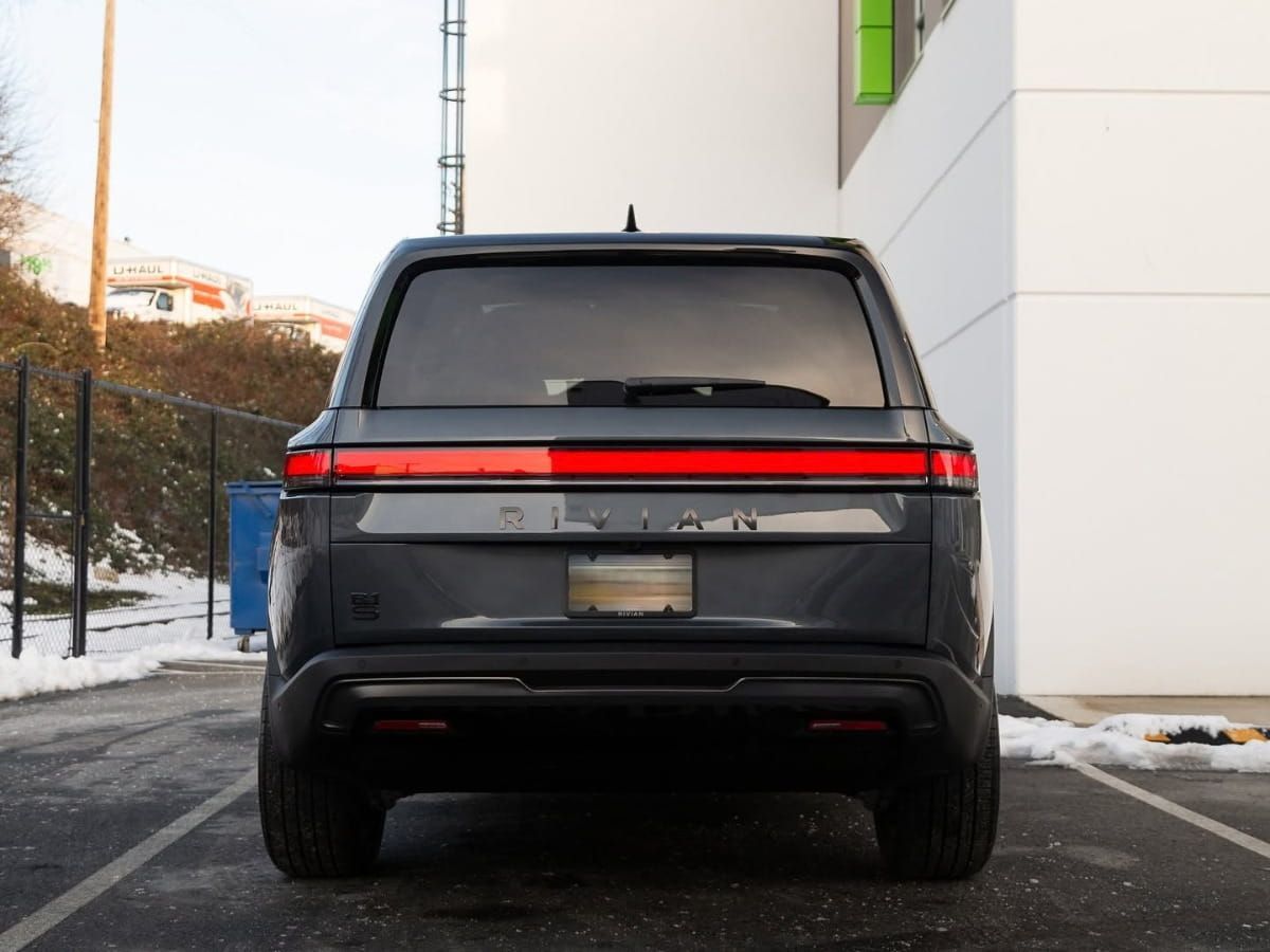 Rear view of a dark SUV parked beside a building with snow along the curb.