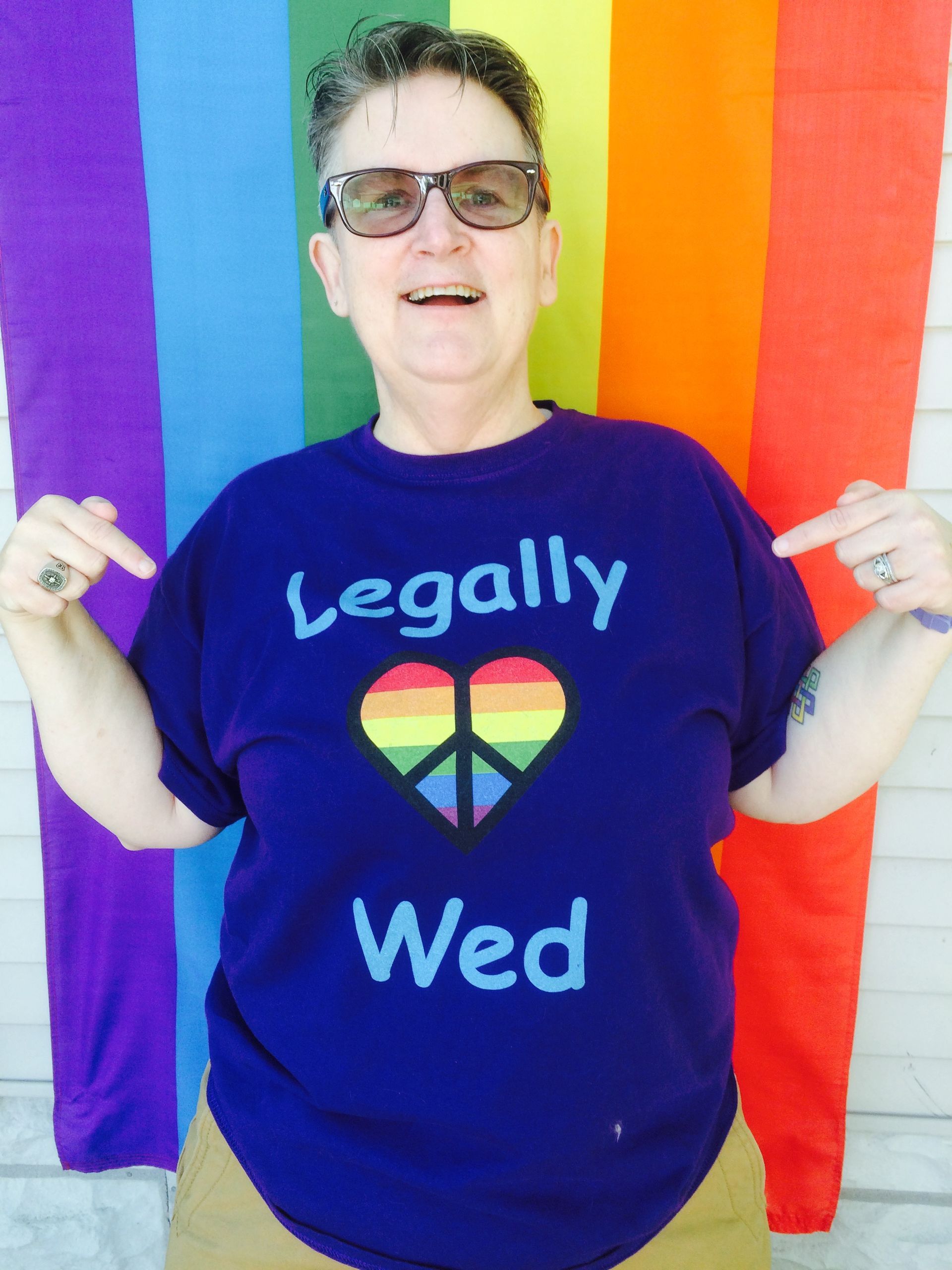 A person smiles, pointing to their shirt that says 