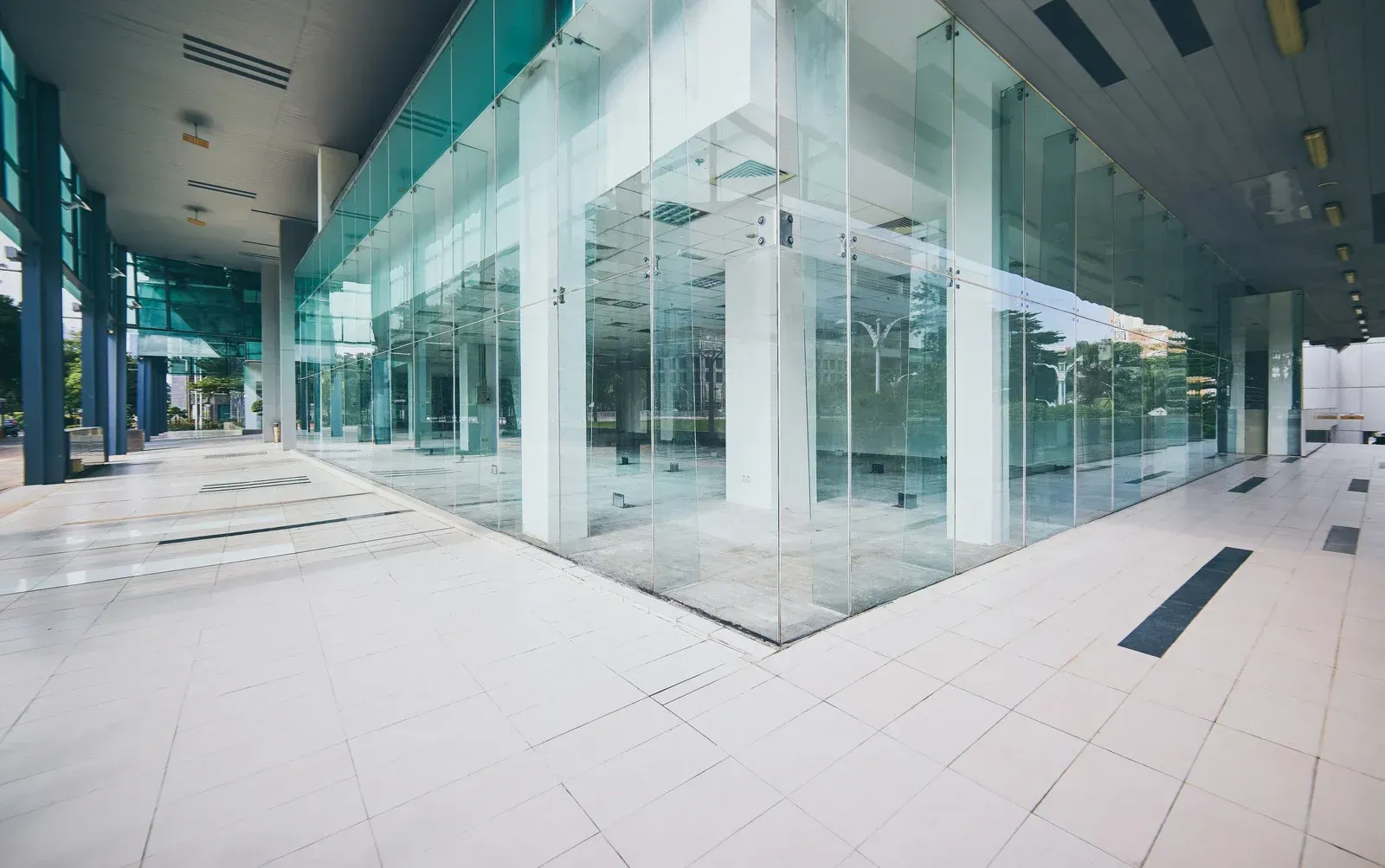 Modern, multi-story office building with large blue-tinted windows, white exterior, palm trees, and clear blue sky.