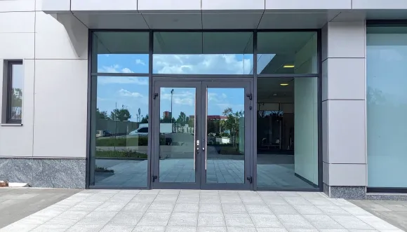 Glass double doors lead into a building with a blue sky reflection.