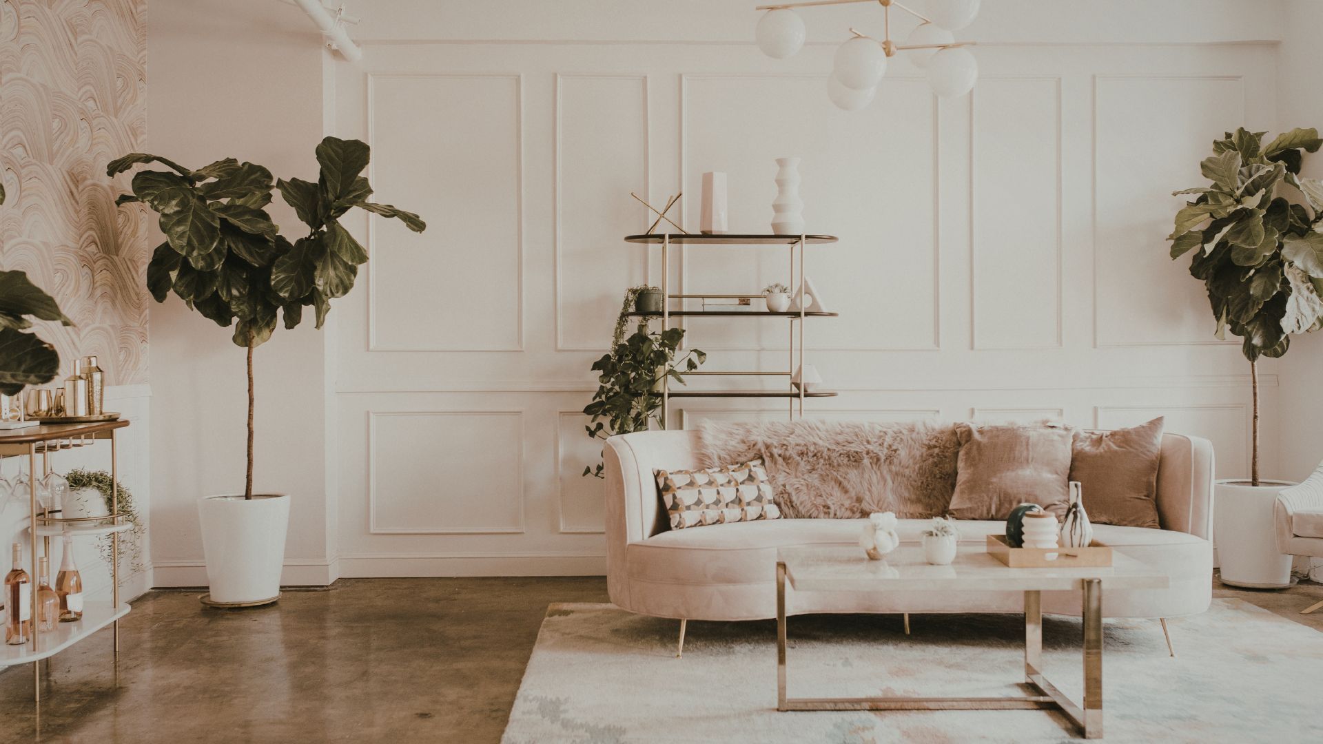 Bright minimalist living room with beige sofa, coffee table, plants, and white paneled walls