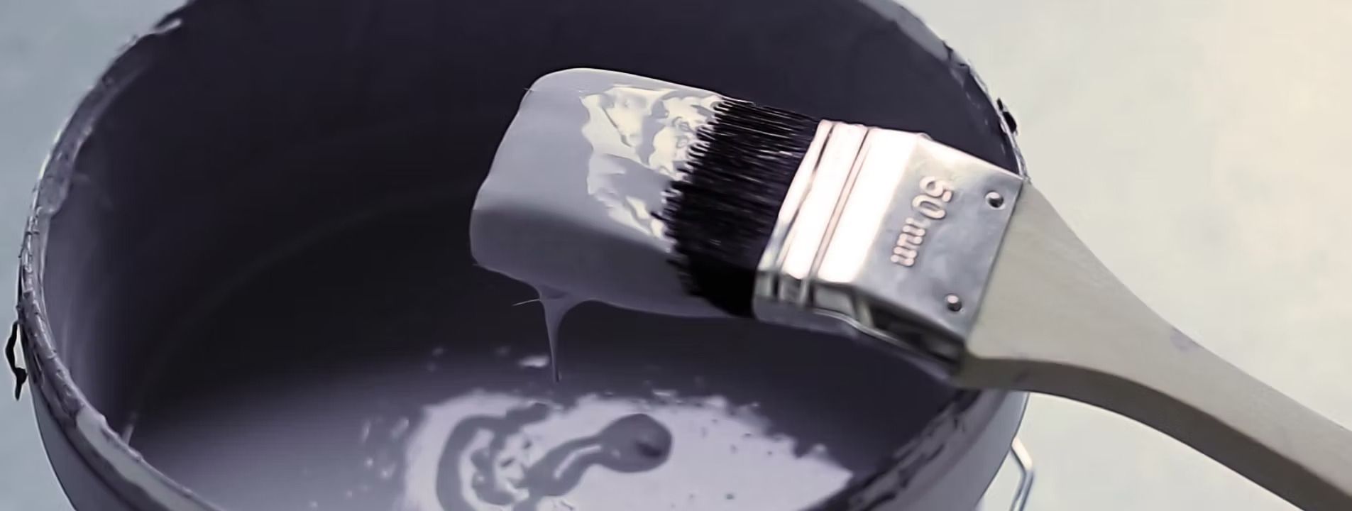 Paintbrush in a black paint can, with dark purple paint being stirred.