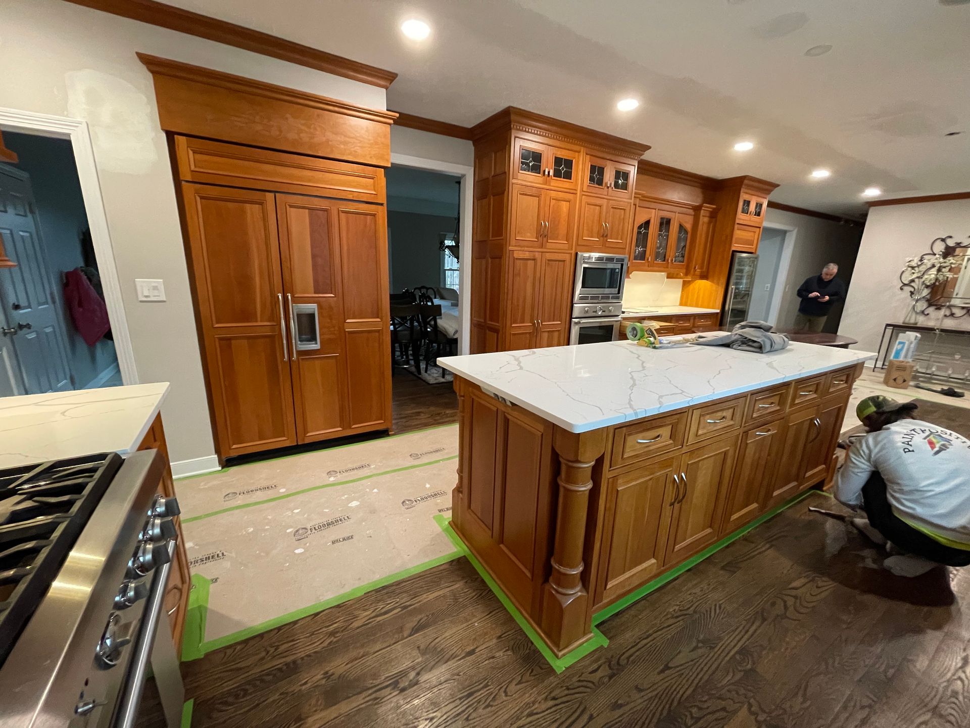 Kitchen under renovation with covered countertops, taped cabinets, and protective floor covering