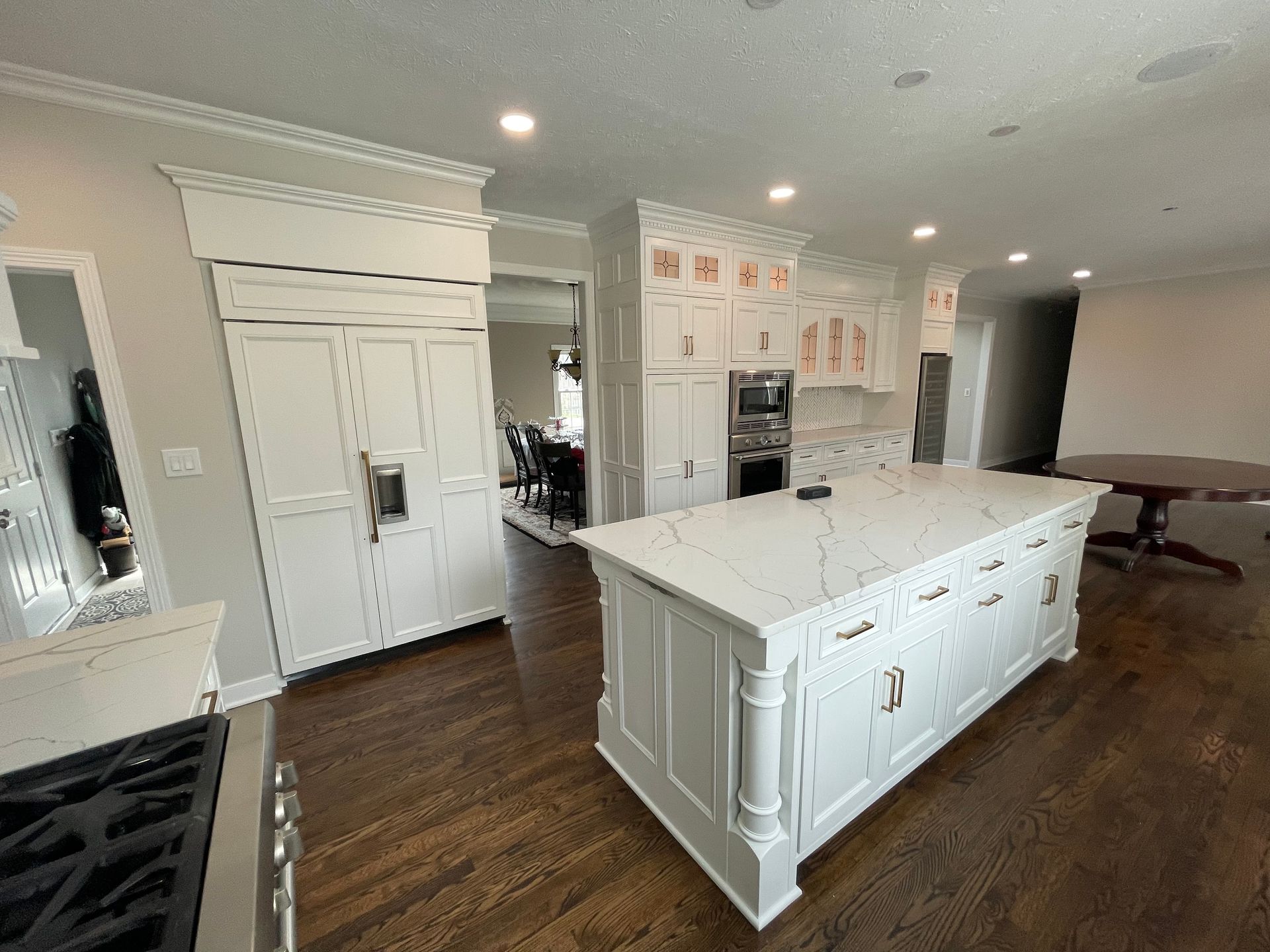 Bright white modern kitchen with a long marble island, dark wood floors, and built-in appliances.
