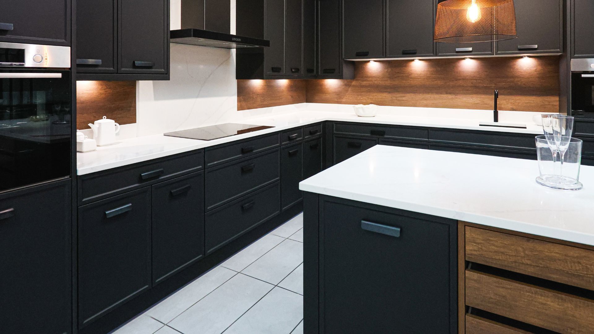 Modern kitchen with dark cabinets, white countertops, and warm under-cabinet lighting