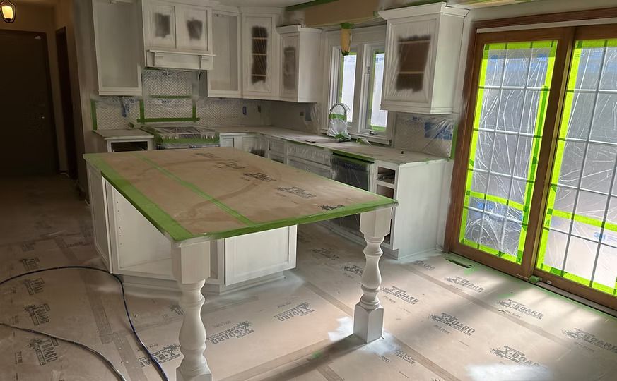 Bright white kitchen with an island and green trim, viewed from the tiled floor near glass doors.