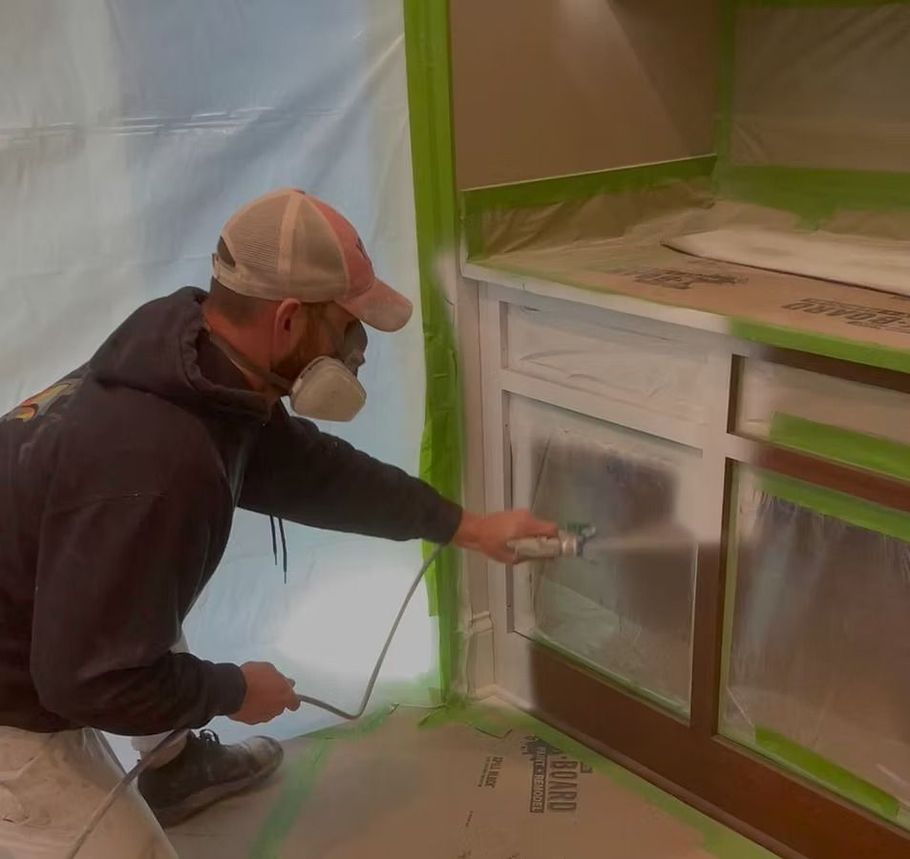 Person spray-painting cabinet doors masked off with green tape in a room under renovation