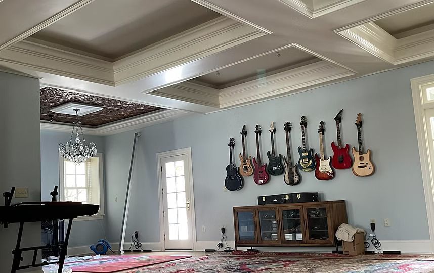 Spacious room with guitars mounted on a wall, a keyboard stand, and large windows under a coffered ceiling.