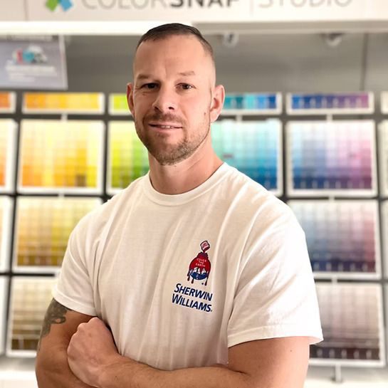 Man standing with arms crossed in front of color swatch displays in a paint store