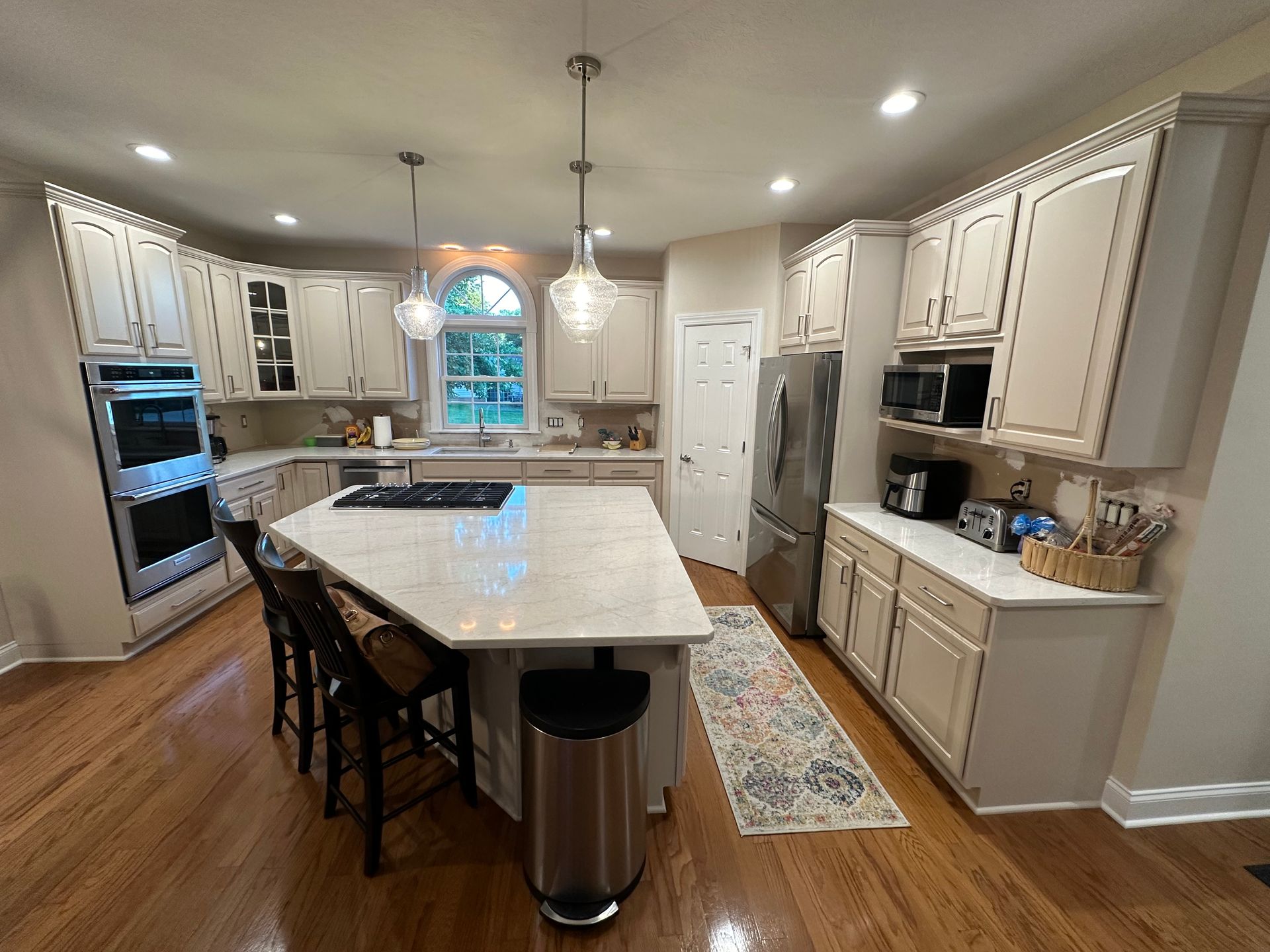 Bright white modern kitchen with a long marble island, dark wood floors, and built-in appliances.
