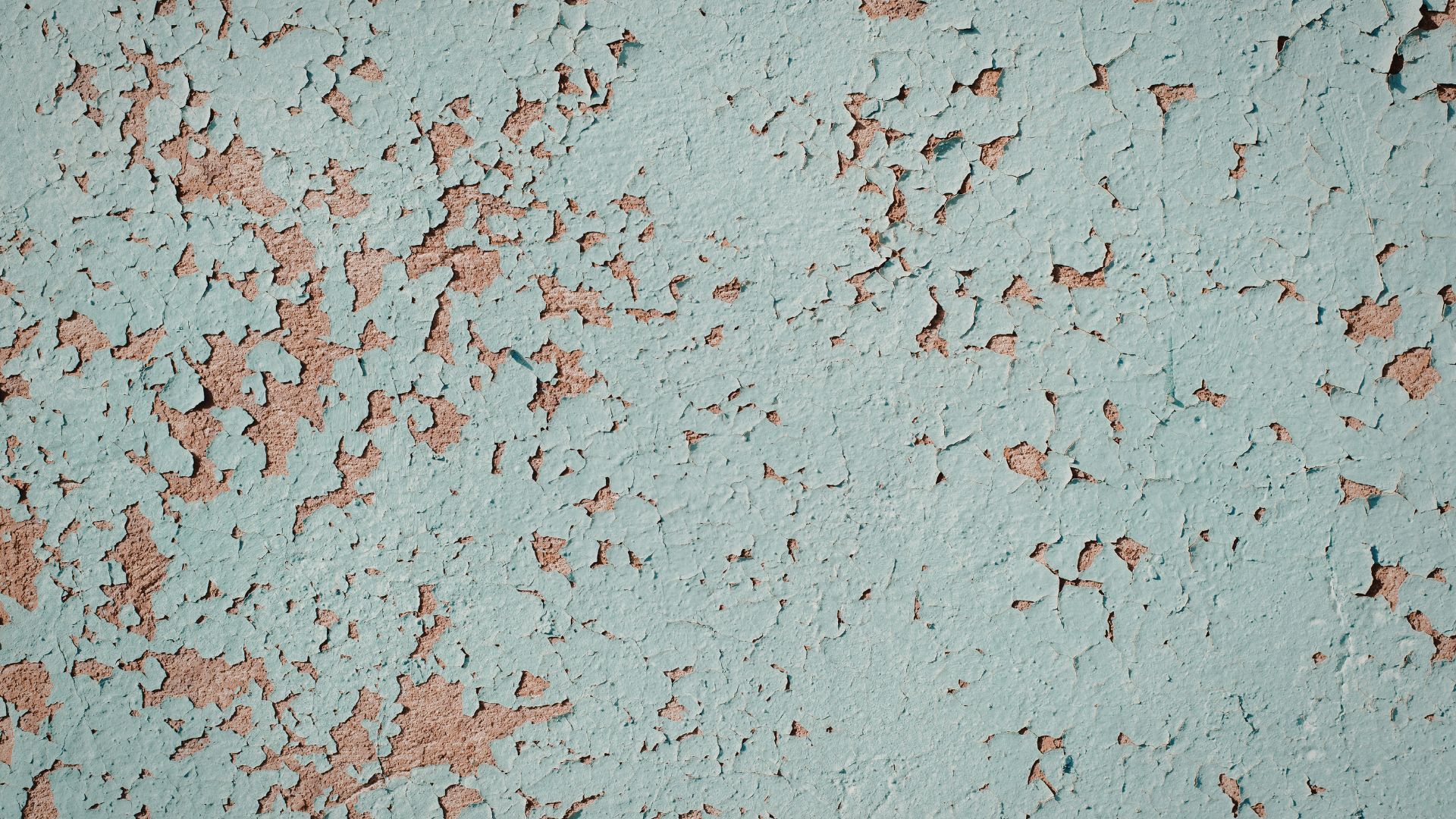 Peeling pale blue paint on a weathered wall with exposed reddish underlayer