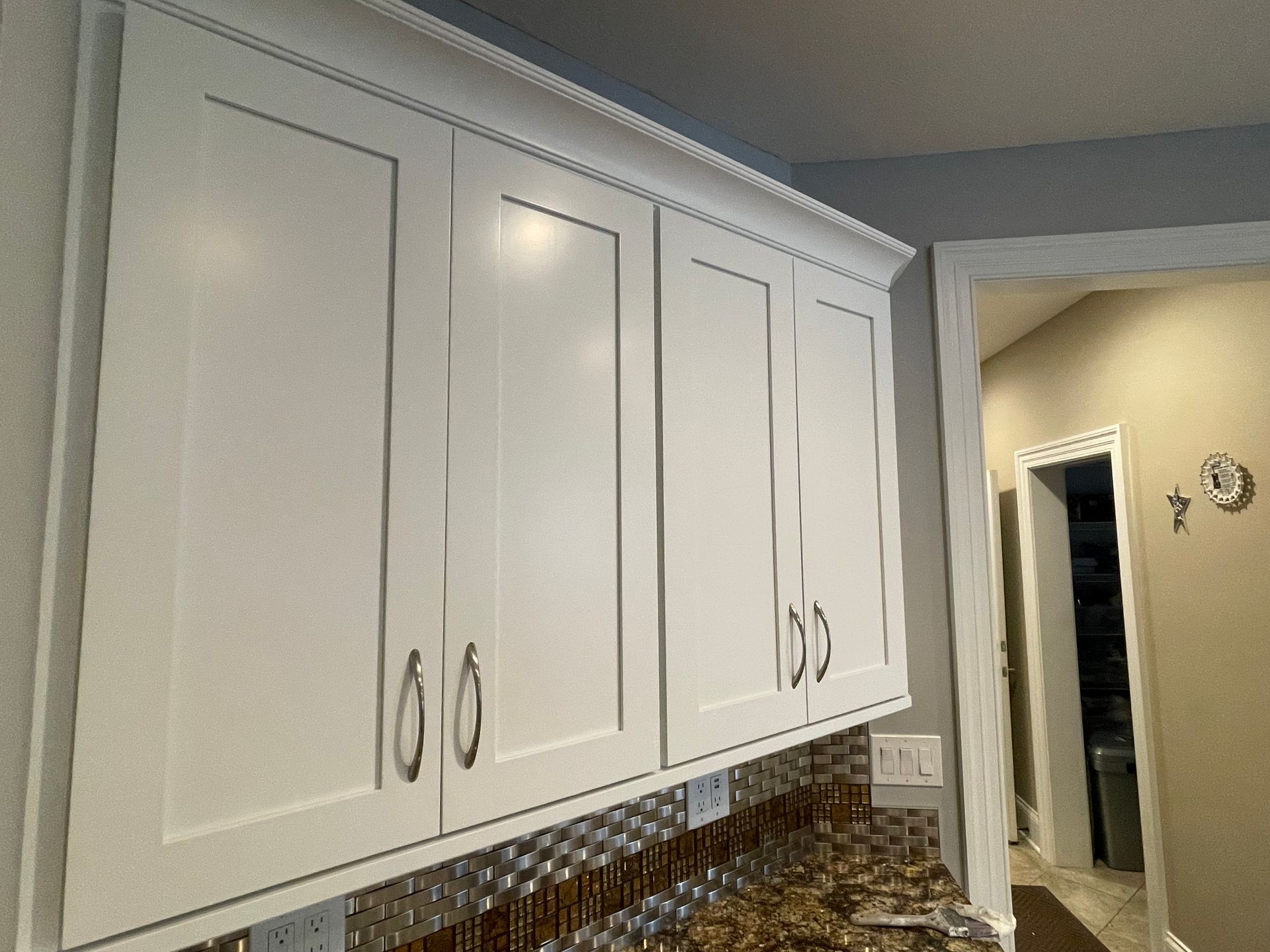Small white kitchen with wooden cabinets, tiled backsplash, stove, sink, kettle, and microwave.