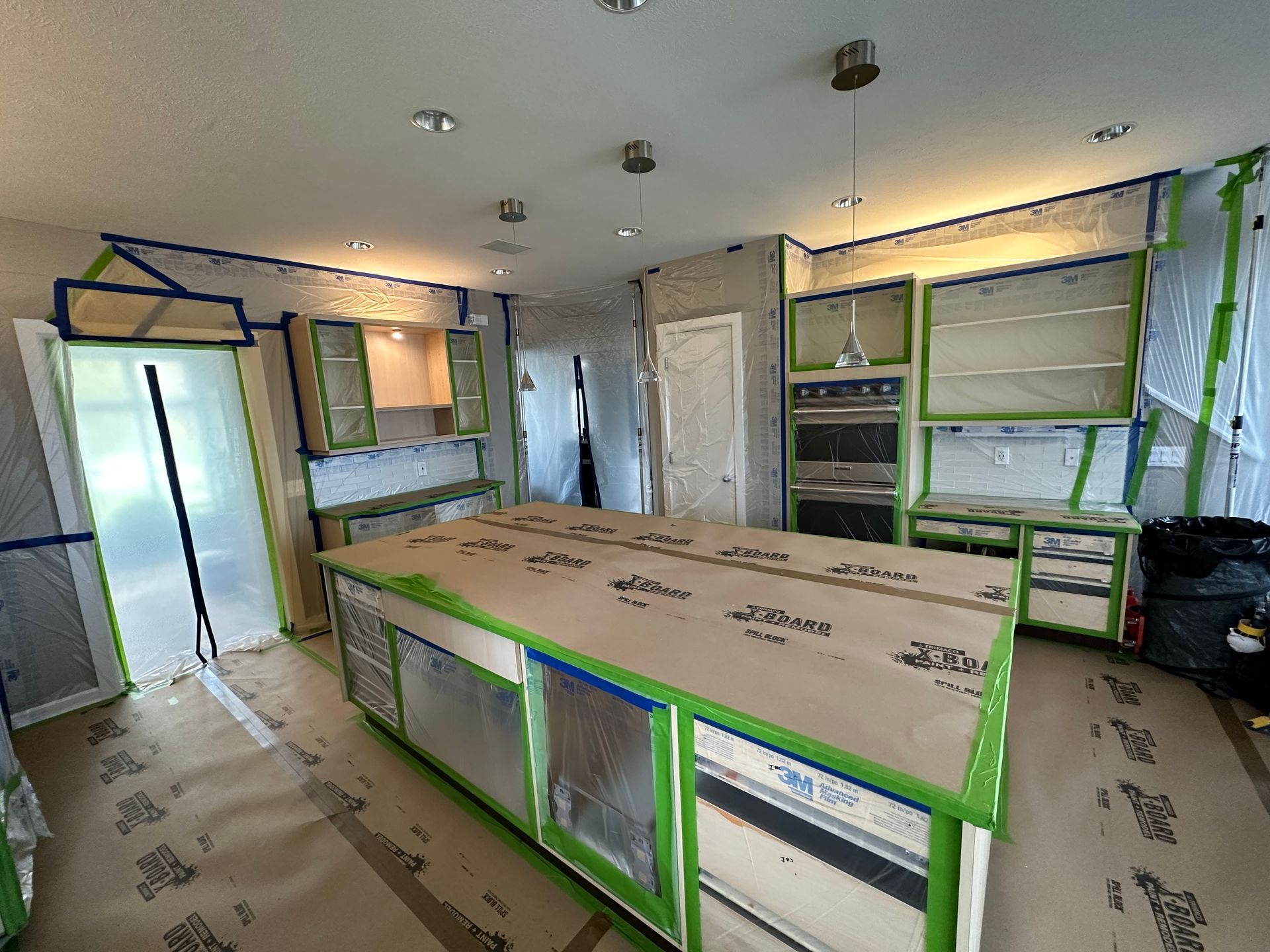 Renovated kitchen with green-trimmed cabinets, countertops, and protective floor coverings
