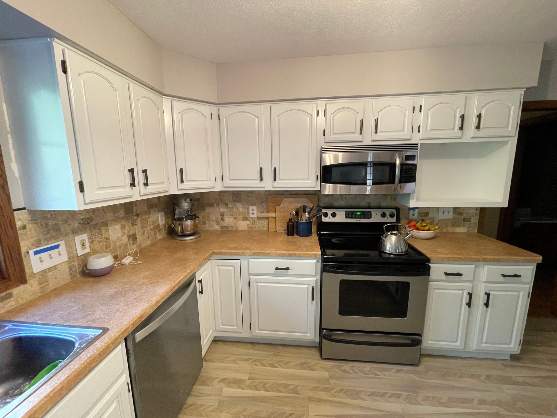 Small kitchen with white cabinets, blue countertop, sink, window, and a table near the left wall.
