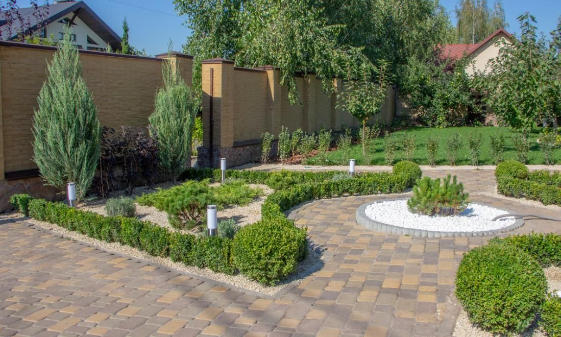 Stone paved garden with manicured hedges, shrubs, and trees.