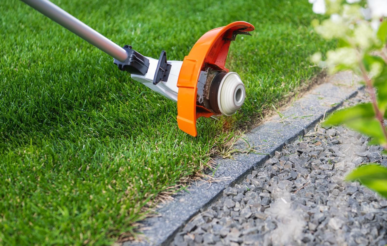 String trimmer edging grass along a gravel walkway.