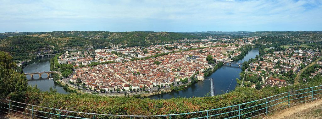 Panoramic aerial view of a riverside city with red-roofed buildings and a curved river