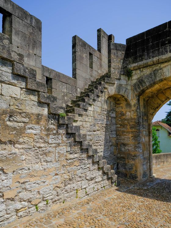 Stone castle wall with a narrow staircase and arched gateway under a blue sky