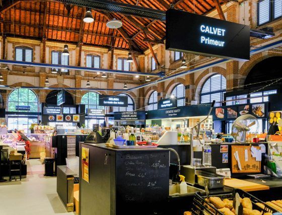 Inside a bright indoor market, a Calvet Primur counter sits beneath a wooden arched ceiling.