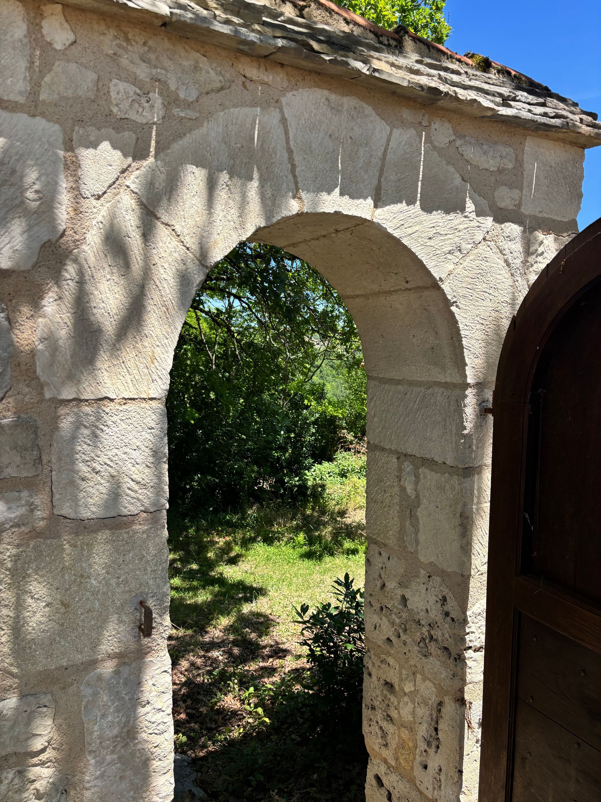 Stone archway in a sunlit garden, with greenery visible beyond the doorway.