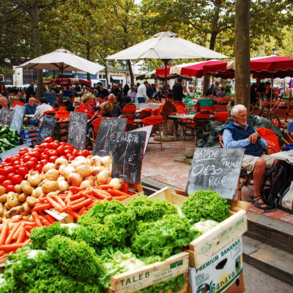A man sits in front of a display of vegetables including lettuce and carrots, market day Fleur de Lys Retreats.